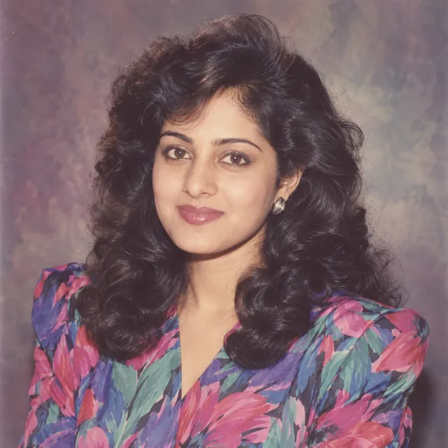1980s-style studio portrait of a young Indian woman with big soft curls and a bright floral blouse with shoulder pads