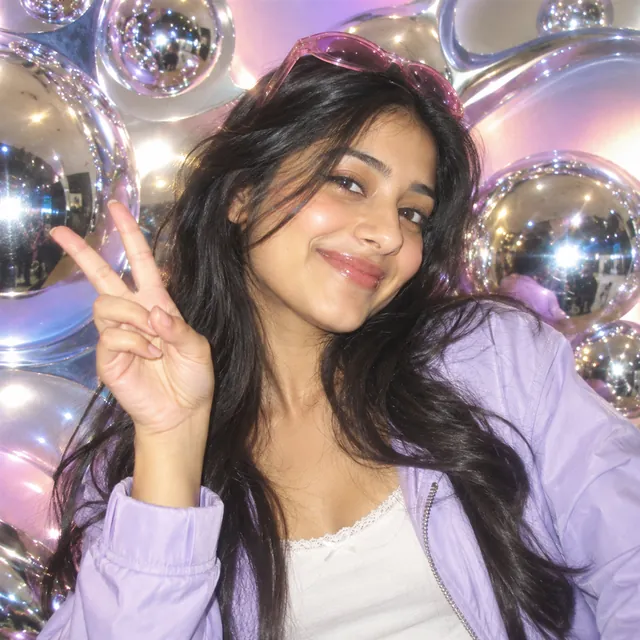 Glossy Y2K-style flash photo of a young woman in a lilac jacket making a peace sign before shiny chrome bubbles